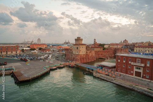 Sunlit harbor in Livorno Italy with historic red walls and distant ships