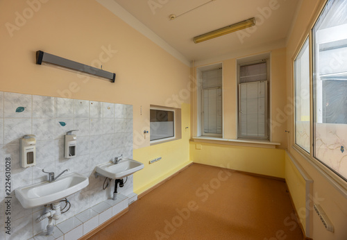 Two wall-mounted washbasins with elbow-operated taps and dispensers stand in a hospital handwashing area