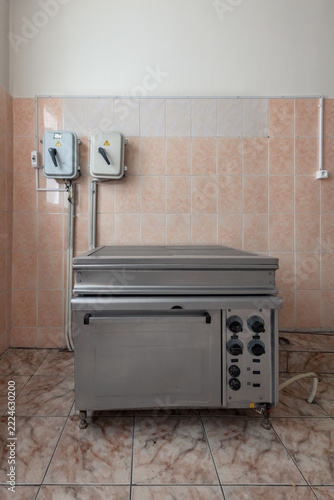 A commercial electric range with an oven and solid hotplates stands against a tiled kitchen wall with copy space above