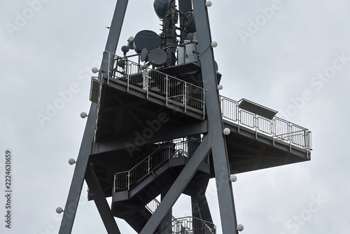 Telecommunication tower with microwave dishes, cell antennas, and observation deck against overcast sky background. Steel communications mast for 5G network coverage, wireless signal broadcasting