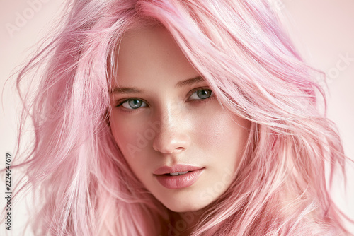 Pastel pink hair beauty portrait of a young woman with glossy flowing waves, natural makeup, luminous skin and soft blush studio background