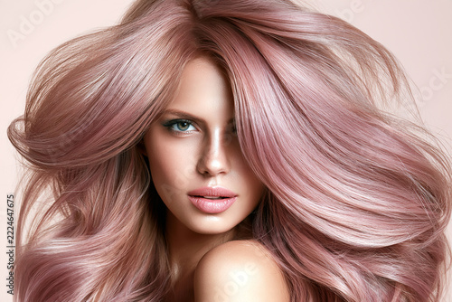 Beauty portrait featuring long pastel pink hair, glossy waves and natural makeup against a soft blush background for salon, cosmetics and fashion campaigns.