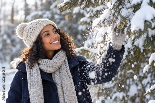 Happy woman brushing snow from an evergreen branch in a winter forest