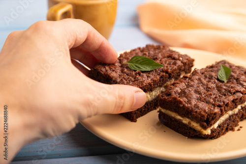 Chocolate cheese cake with cup of coffee with hand on blue wooden, close up, side view, selective focus