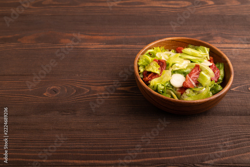 Mixed salad with lettuce, tomatoes in wooden bowl on brown wooden. side view, copy space