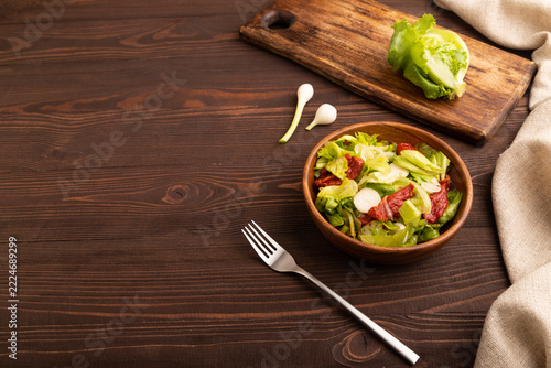Mixed salad with lettuce, tomatoes, onion in wooden bowl on brown wooden. side view, copy space