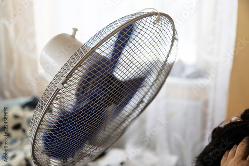 A close-up view shows a rotating electric fan with blue blades protected by a metal wire cage.