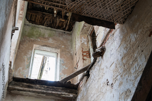 The interior of an old abandoned building reveals crumbling walls, exposed wooden beams, and a damaged ceiling.