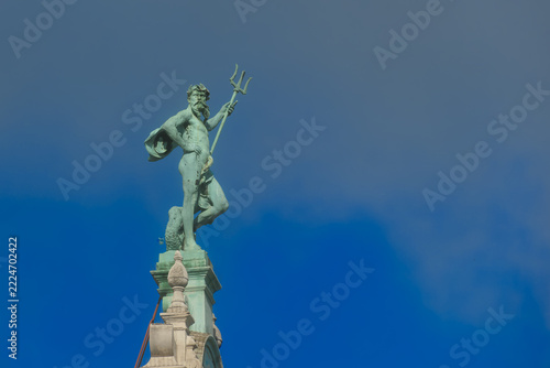 A striking Antwerp rooftop figure of Poseidon standing high above the street, holding a trident and draped in a cloak, his bronze form set sharply 