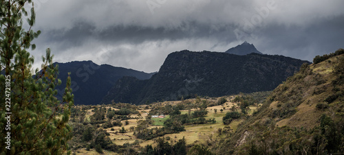 Fotografie Paisaje de colinas rurales con casas dispersas y cordillera de montañas bajo cie