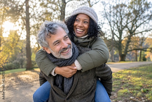 Smiling man giving a woman a piggyback ride in a softly lit winter park
