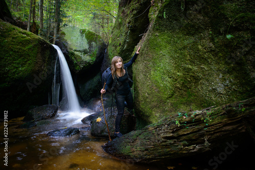 Young female hiker with backpack and walking stick standing by picturesque waterfall in Ysperklamm gorge Austria