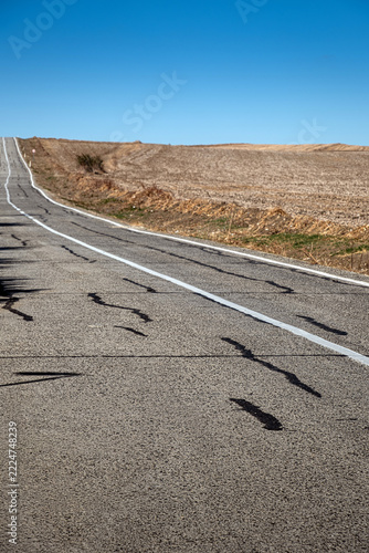 An old and worn asphalt road in a rural area. agricultural lands and blue sky background. 