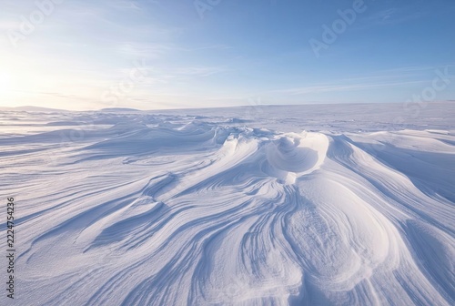 Snowdrifts with smooth wind sculpted patterns stretching across a vast frozen tundra under a clear blue sky.