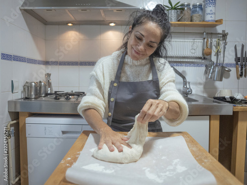 Smiling mature woman kneading fresh dough on a wooden table in the kitchen
