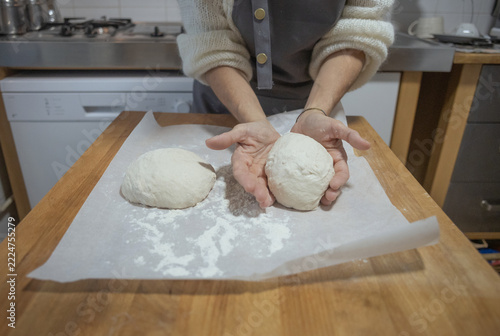 Close-up of female hands shaping and holding fresh raw bread dough balls on a kitchen table