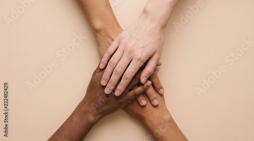 Top view of four hands with different skin tones stacked together showing unity, diversity, and teamwork