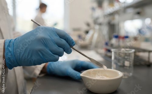 Scientist in blue gloves mixing powder with spatula in a laboratory setting for pharmaceutical research