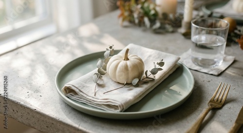 White miniature pumpkin on a green plate with napkin and eucalyptus on a concrete table