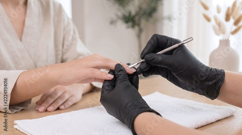 Technician pushing cuticle on woman in nail salon during manicure