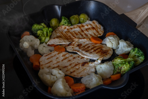 Lean chicken breasts cooking with broccoli, cauliflower, carrots, and brussels sprouts in a grill pan, preparing a nutritious and balanced low-fat meal