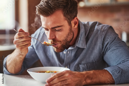 Ein Mann sitzt am Tisch und löffelt seine Suppe aus einer Essensschüssel