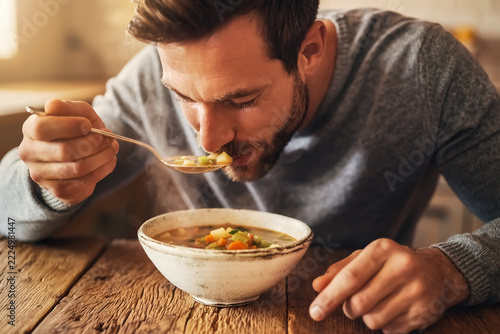 Ein Mann sitzt am Tisch und löffelt seine Suppe aus einer Essensschüssel