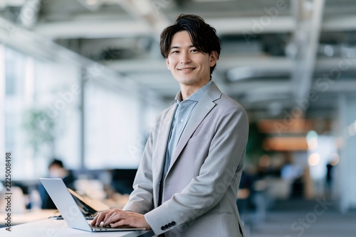 オフィスで働く若手ビジネスマンが笑顔でノートパソコンを使用