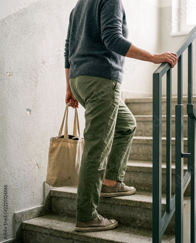 Person climbing concrete stairs holding handrail and canvas tote bag