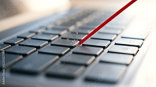 Compressed air being sprayed from a red nozzle to clean dust and debris between the keys of a laptop keyboard.