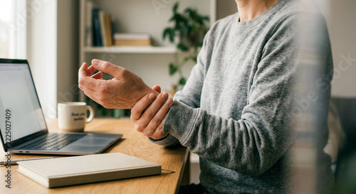Senior person holding painful wrist at home office desk