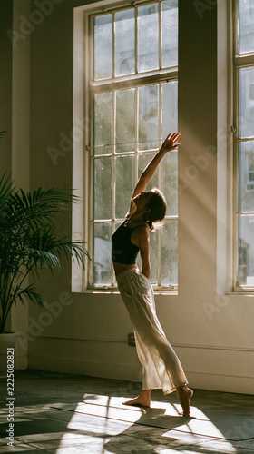 Woman Doing Yoga Stretch by Large Window in Morning Light - Arms Raised