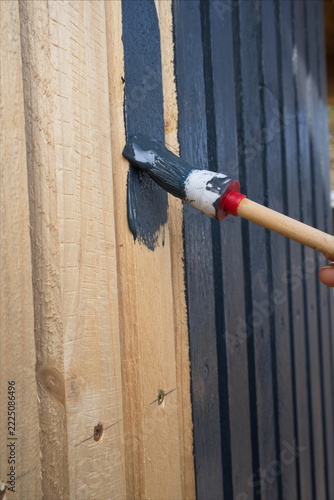 Streichen einer Holzoberfläche – links naturbelassen, rechts bereits dunkel gestrichen. Ein Pinsel trägt frische Farbe auf die Holzplanken auf.