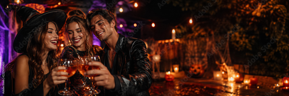 Naklejka premium Friends in Halloween costumes toasting drinks at an outdoor party. Halloween celebration and seasonal festivities. Costume party, social gathering and holiday nightlife.