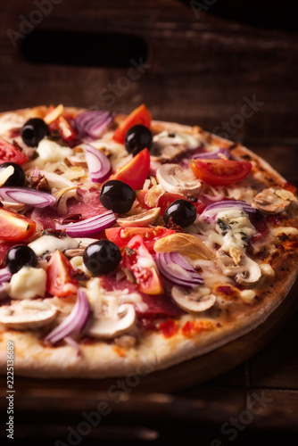 Pizza with salami, cherry tomatoes and mozzarella cheese. Rustic wooden background. Soft focus. Close up.
