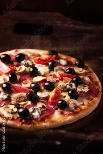 Pizza with salami, cherry tomatoes and mozzarella cheese. Rustic wooden background. Soft focus. Close up.