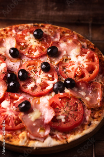 Pizza with ham, mozzarella cheese and tomatoes . Rustic wooden background. Soft focus.