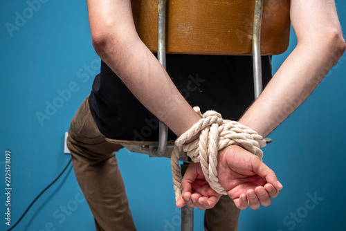 Obraz na plátně A man's hands are tied with a rope and he is sitting on a chair.