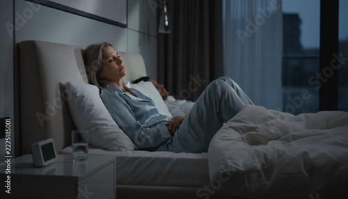 Woman Awake in Bed at Night, Early Menopause Symptoms and Insomnia.  Mature woman lying awake in bed at night suffering from insomnia, hot flashes and sleep disorder
