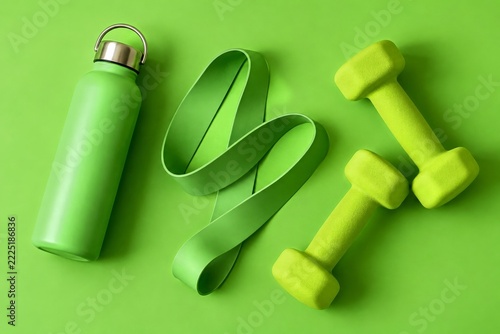 Green bottle resistance band and lime dumbbells on a matching green background