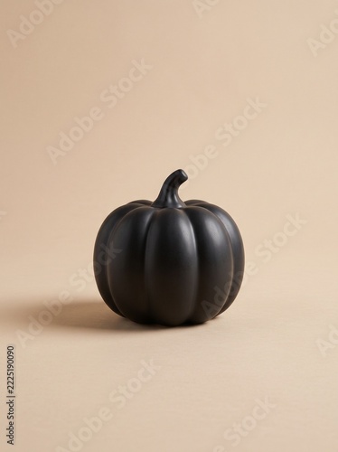 Matte black ceramic pumpkin with curved stem on beige background, minimalist modern Halloween decor
