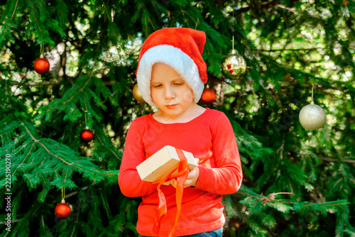 Child kid waiting for Christmas.little boy opening gift box near fir tree.winter festive holidays,family.Merry Christmas eve,New Year,Happy Holidays