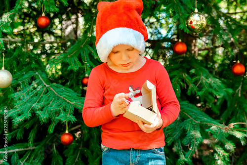 Child kid waiting for Christmas.little boy opening gift box near fir tree.winter festive holidays,family.Merry Christmas eve,New Year,Happy Holidays