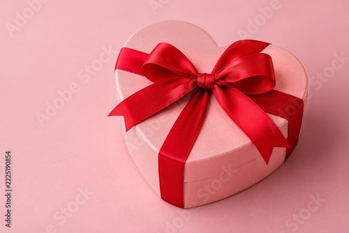 Pink heart shaped gift box tied with a red satin ribbon on a pastel background