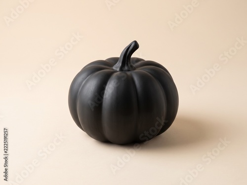 Large matte black ceramic pumpkin with ribbed shape and curved stem on cream beige background, horizontal Halloween still life