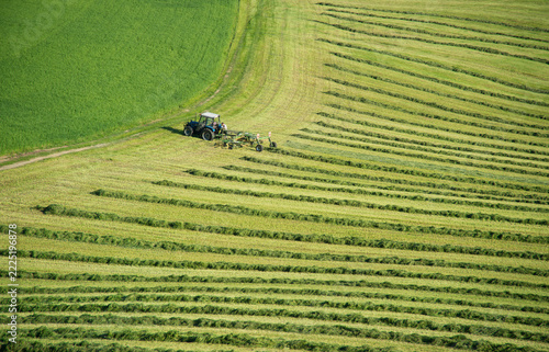 High angle view of tractor raking freshly cut grass into neat swaths on green farmland