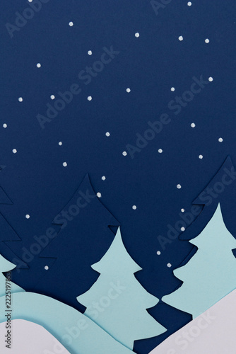 Winter landscape made from layered paper, with snowy mountains, paper trees, and illustrated snow on a dark blue background. Winter concept for graphic design and seasonal creative projects