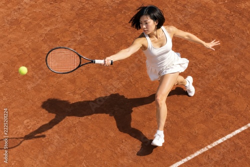 Overhead female tennis player swinging on a clay court with a sharp shadow