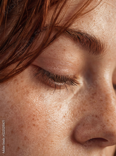 Extreme close-up of freckled skin, closed eye and eyelashes on redhead woman