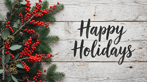 Happy holidays greeting card with red berries and pine branches on rustic wooden background